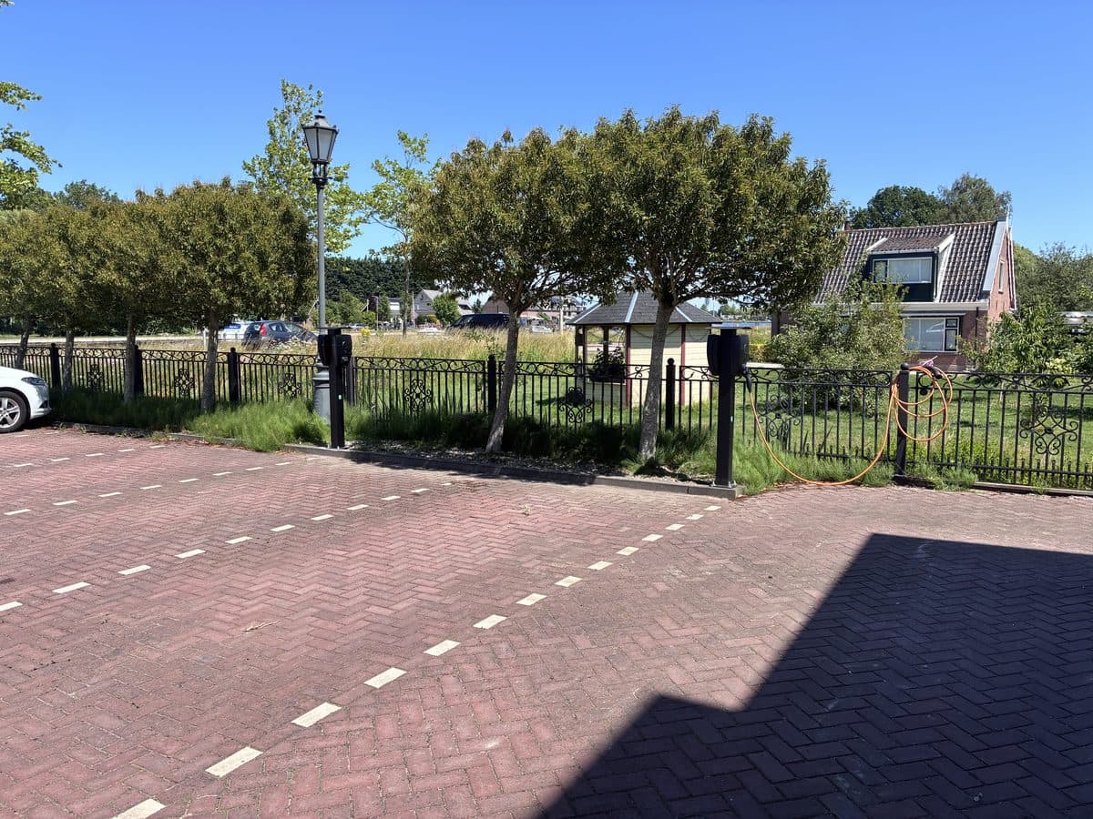 Twee laadpalen op een parkeerplaats langs een hek, op een zonnige dag